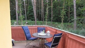 Un patio techado al aire libre con una mesa redonda y sillas azules, rodeado por una terraza de madera y una barandilla roja.