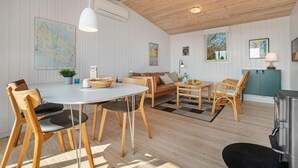 Een moderne woonkamer met een ronde eettafel, houten stoelen, een bank en een salontafel. Op de muur hangt een kaart, er staat een lamp en een kleine plant.