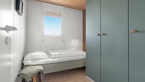Een slaapkamer met een bed, een raam, een kledingkast en een klein tafeltje met een plaid.