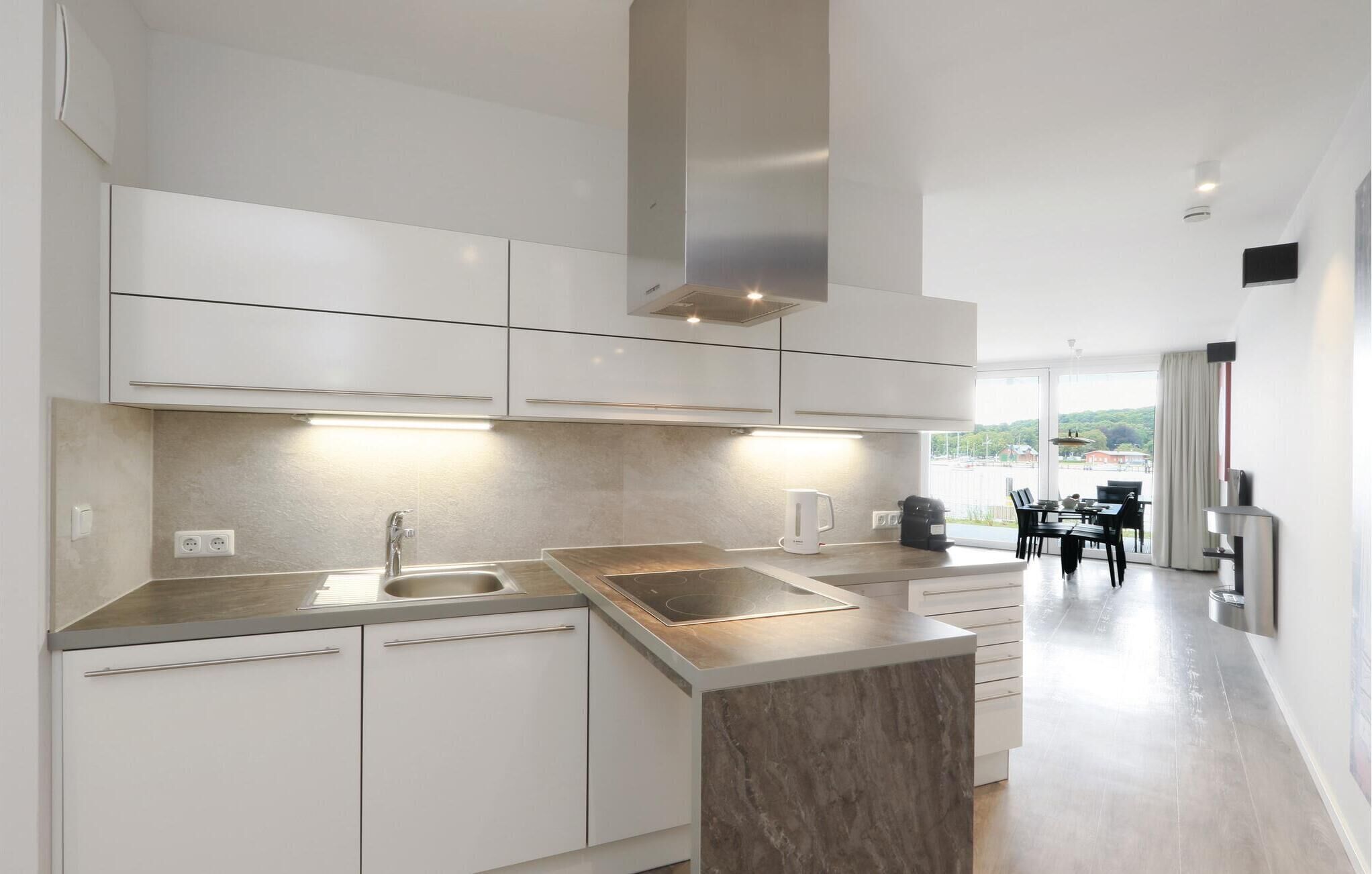 A modern kitchen with white cabinetry, a central island, and a dining area with a view.