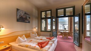 Camera d'albergo con due letti, un'area pranzo e ampie finestre.