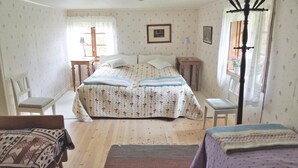 Une chambre à coucher comprenant un lit, deux tables de chevet, une chaise, une fenêtre avec des rideaux, un tableau au mur et un ventilateur de plafond.