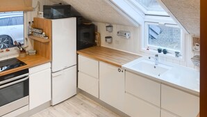 Cozinha compacta com micro-ondas, fogão e pia. Apresenta um claraboia e bancadas de madeira.