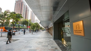 Un hotel moderno con un paseo cubierto, ventanas amplias y un cartel que indica que es un hotel de llegadas.