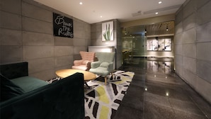 A modern lobby with a seating area featuring a green sofa, a wooden table, and patterned chairs. A sign reads "Break the Rules."