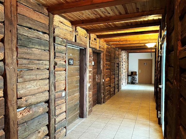 A corridor with wooden walls and a tiled floor, leading to a room with a door and a small table.