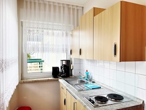 A compact kitchen with wooden cabinets, a coffee maker, a kettle, and a stove.