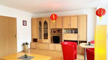 A modern living room with a wooden cabinet, a red sofa, and a dining table.