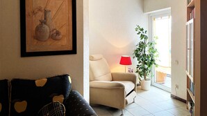 Una sala de estar con un sofá, un sillón, una lámpara, una planta en maceta y una obra de arte enmarcada en la pared.