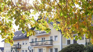 Un edificio de varios pisos con balcones, un letrero que dice "Silbersee Haus" y una cerca verde al frente.