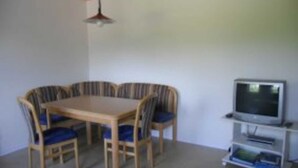 A dining area with a wooden table and six chairs, a television on a stand, and a ceiling light. - Apartment 1 - Budach: Country vacation at the gates of Flensburg (Handewitt)