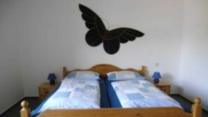 A wooden bed with a blue and white duvet, two bedside tables with lamps, and a wall-mounted butterfly decoration. - Apartment 1 - Budach: Country vacation at the gates of Flensburg (Handewitt)
