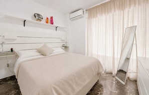 A hotel room with a bed, bedside table, lamp, air conditioning unit, and a large mirror. - Beach front apartment in Torrevieja with WiFi (Torrevieja)