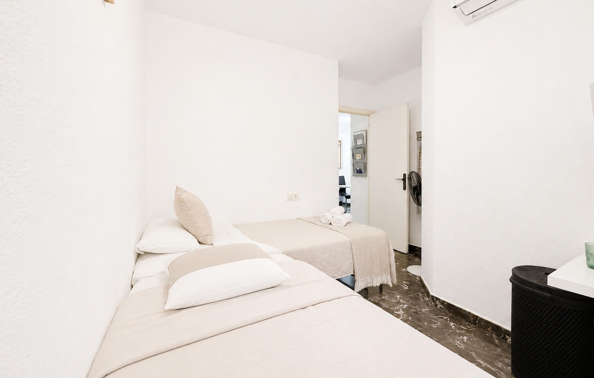 Ein schmales Hotelzimmer mit zwei Betten, einem kleinen Badezimmer und einem Mülleimer.