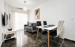 A modern living room with a dining area, a sofa, a TV, and a painting on the wall. - Beach front apartment in Torrevieja with WiFi (Torrevieja)