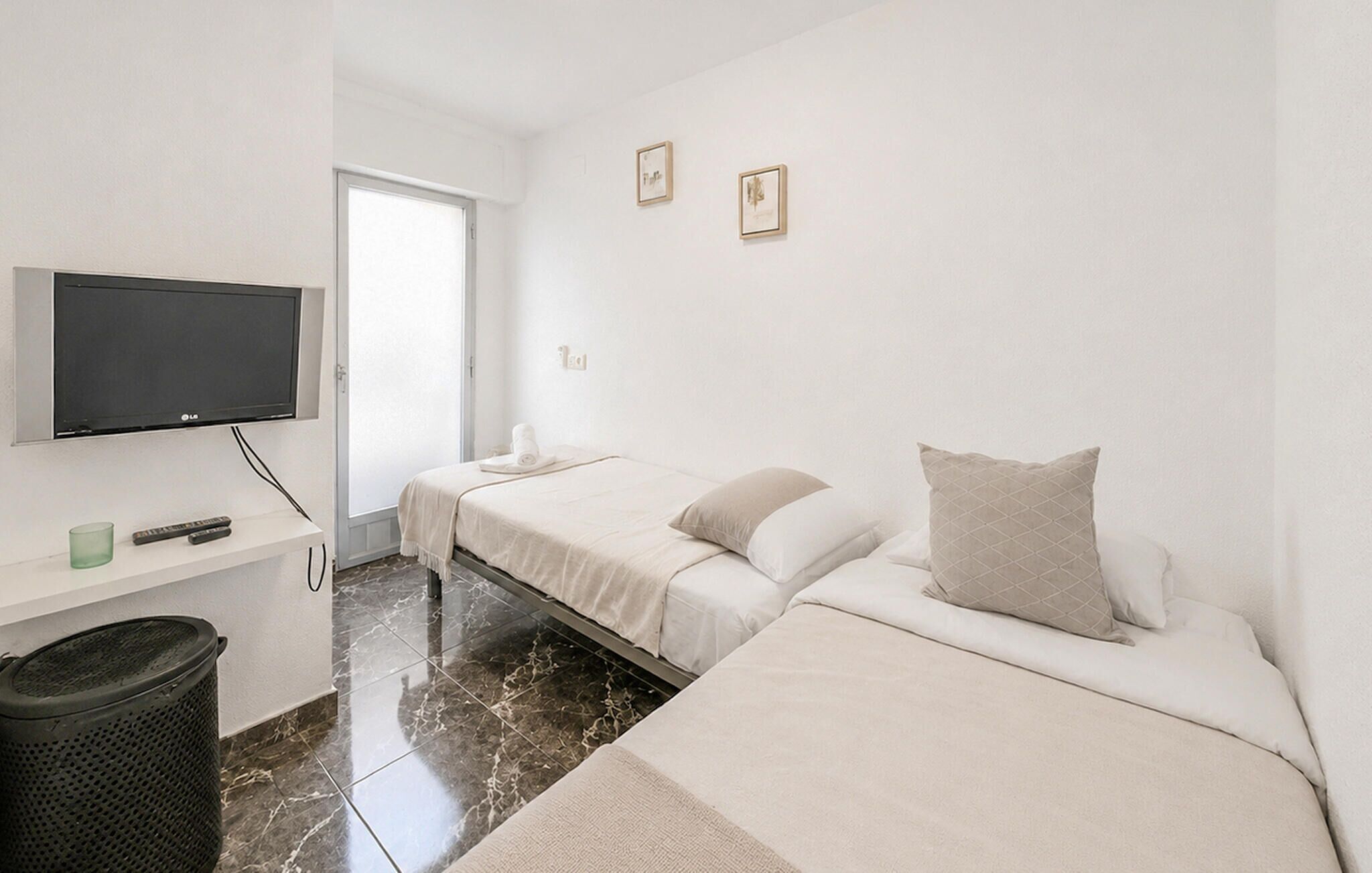 A hotel room with two beds, a TV, a trash bin, and a door leading to a balcony.