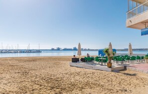A beachside café with outdoor seating, a view of the sea, and a distant industrial area. - Beach front apartment in Torrevieja with WiFi (Torrevieja)