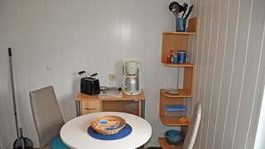 Pieni, käytännöllinen keittiö, jossa on pyöreä pöytä, tuolit, kahvinkeitin ja luuta.