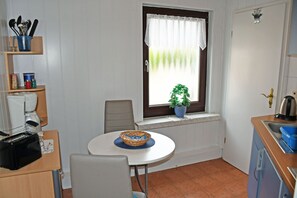 A compact kitchen with a dining table, chairs, a coffee machine, a sink, and a window with a plant. - 02 Holiday apartment with terrace - Holiday apartments with terrace in Ostseebad Sellin (Sellin)
