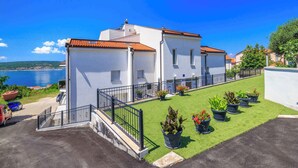Un edifici blanc amb teules vermelles, un petit jardí amb plantes en testos i vista al mar.