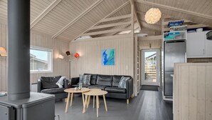 A cozy cabin interior with a black leather sofa, a wooden coffee table, a modern stove, and a wooden ceiling.
