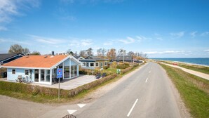 A coastal road with houses, a blue sign indicating a parking area, and a view of the sea.