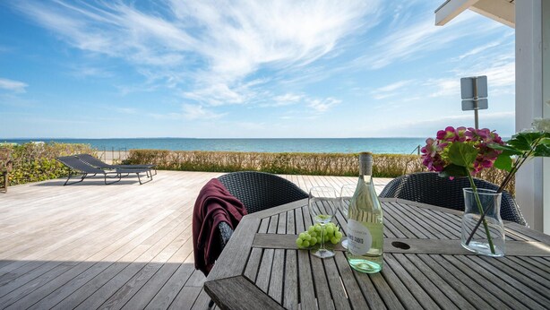 A wooden deck with a table set for dining, overlooking a beach.