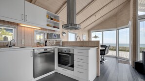 A modern kitchen with white cabinetry, stainless steel appliances, and a large window overlooking the beach.
