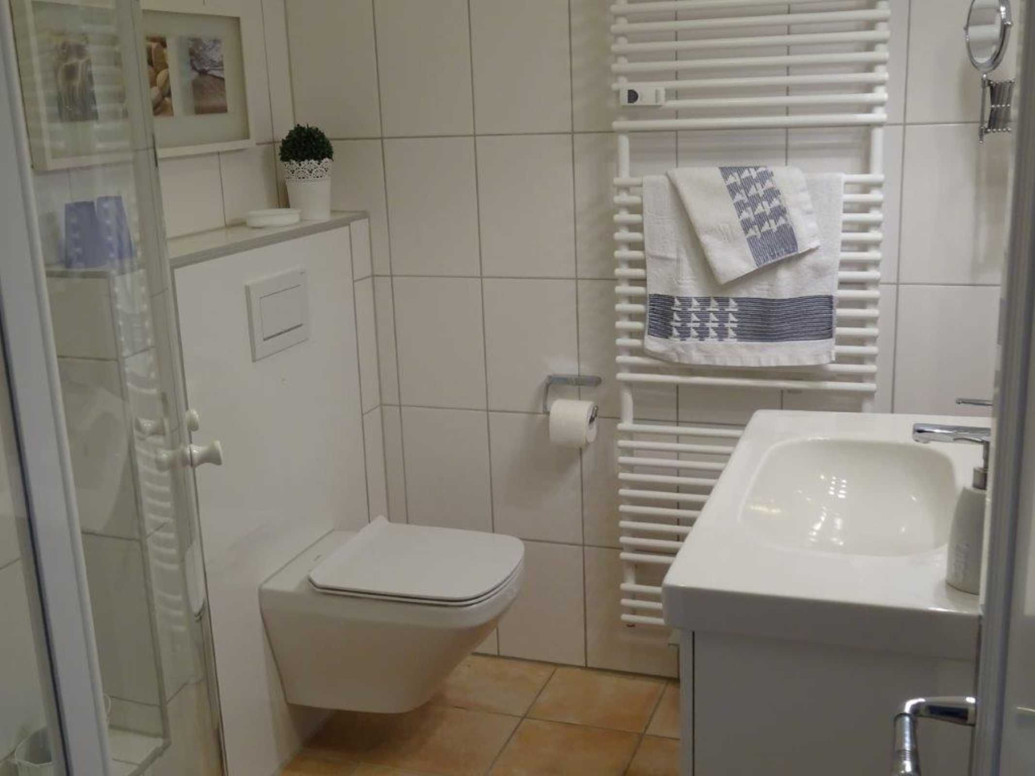 Een badkamer met toilet, wastafel, handdoekrek met handdoek en een kleine potplant op het aanrecht.