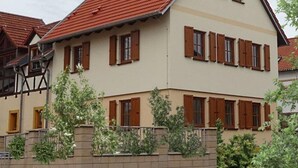 A two-story building with a red-tiled roof, multiple windows with wooden shutters, and a brick wall in front.