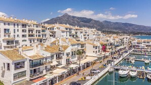 Une ville côtière aux bâtiments blancs, dotée d’un port de plaisance et bordée de montagnes.