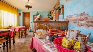A dining area with wooden tables and chairs, a buffet table with baskets of food, and a rustic wall with a mural. - 3 bedroom cozy home in Marsaglia CN (Marsaglia CN)