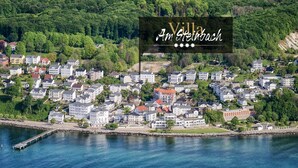 Vista aérea de Villa Am Steinbach, mostrando una propiedad frente al agua con varios edificios, un muelle y abundante vegetación.