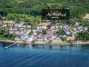Vista aérea de Villa Am Steinbach, mostrando una propiedad frente al agua con varios edificios, un muelle y abundante vegetación.