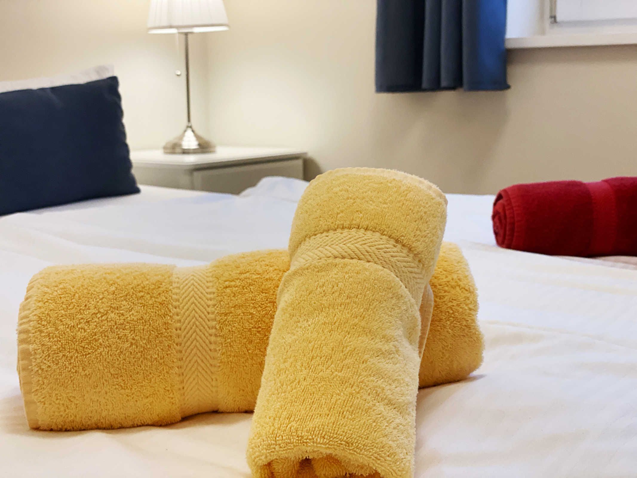 Sängyllä on siististi taitetut pyyhkeet, lamppu ja yöpöytä.