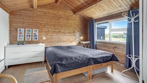 Una camera da letto con pannelli in legno, un letto, un comò e una finestra con tende.