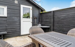 Een terras met rieten meubels, een witte deur en een kleine tafel.