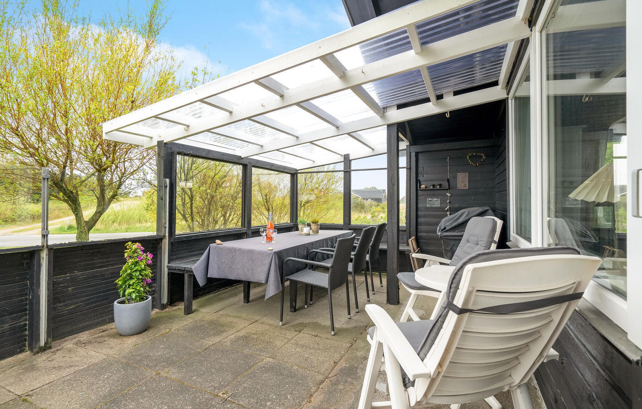 Une terrasse extérieure avec une table et des chaises, un pot de fleurs et une vue sur les arbres et les bâtiments.