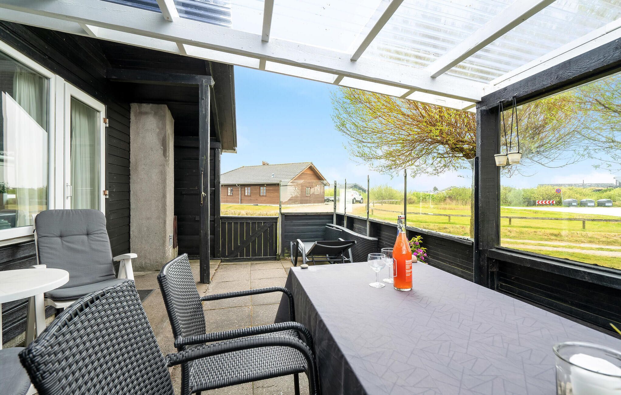 A covered outdoor seating area with wicker furniture and a table, overlooking a rural landscape.