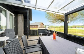 Een overdekt terras met rieten meubels en een tafel, met uitzicht op een landelijk gebied.