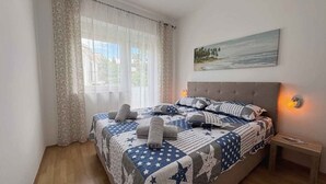 Un dormitori amb un llit, una tauleta de nit, un quadre i una finestra amb cortines.