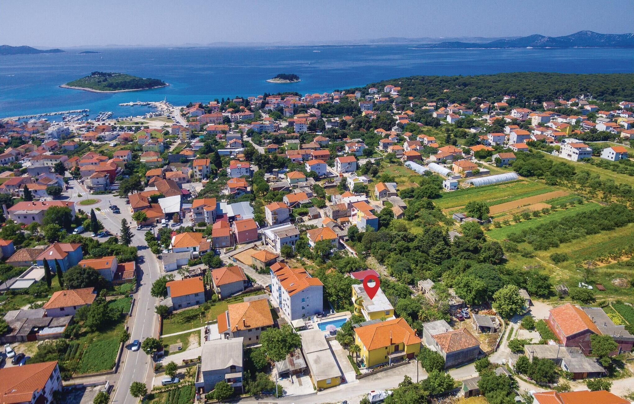 An aerial view of a coastal town with numerous houses, a marina, and green fields.