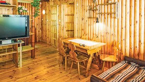 Interior de una cabaña de madera con una mesa de comedor, sillas, un televisor y un sofá.