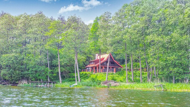 Una cabaña rodeada de un bosque frondoso y un lago.