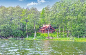 A cabin surrounded by dense forest and a lake.