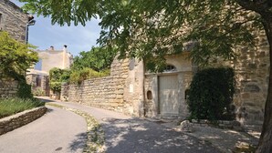 Una estrecha calle empedrada flanqueada por edificios de piedra, un muro de piedra y una reja de metal.