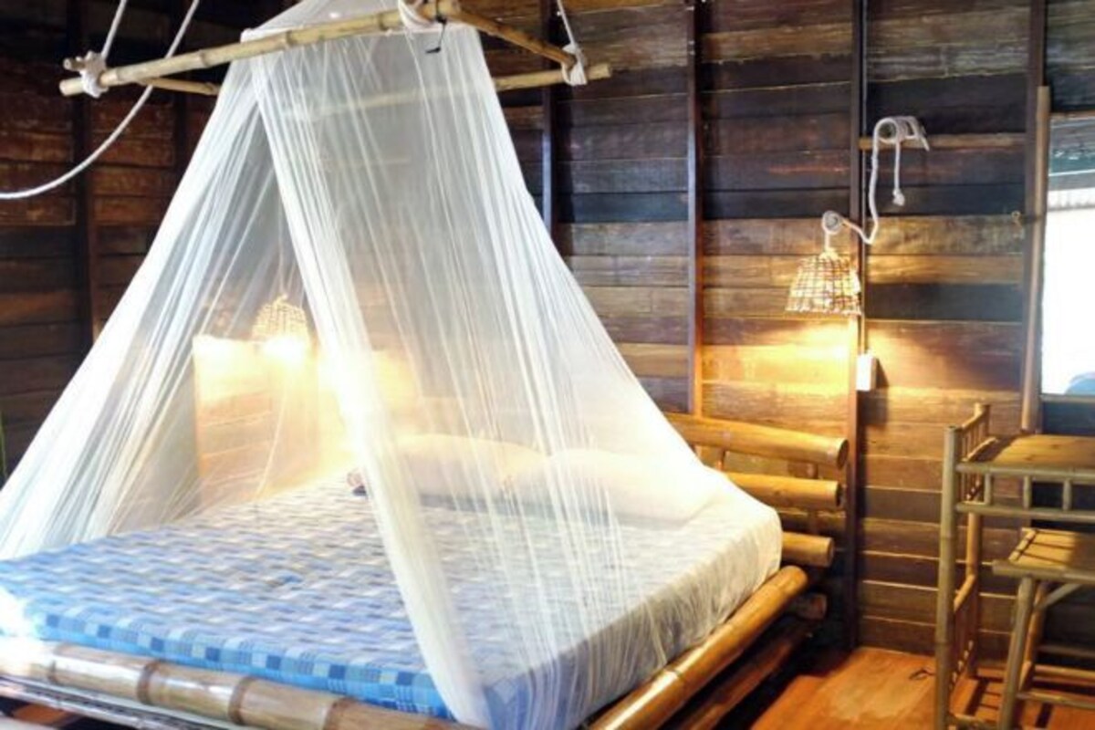 Una cama con mosquitero, paredes de madera y una luz nocturna.
