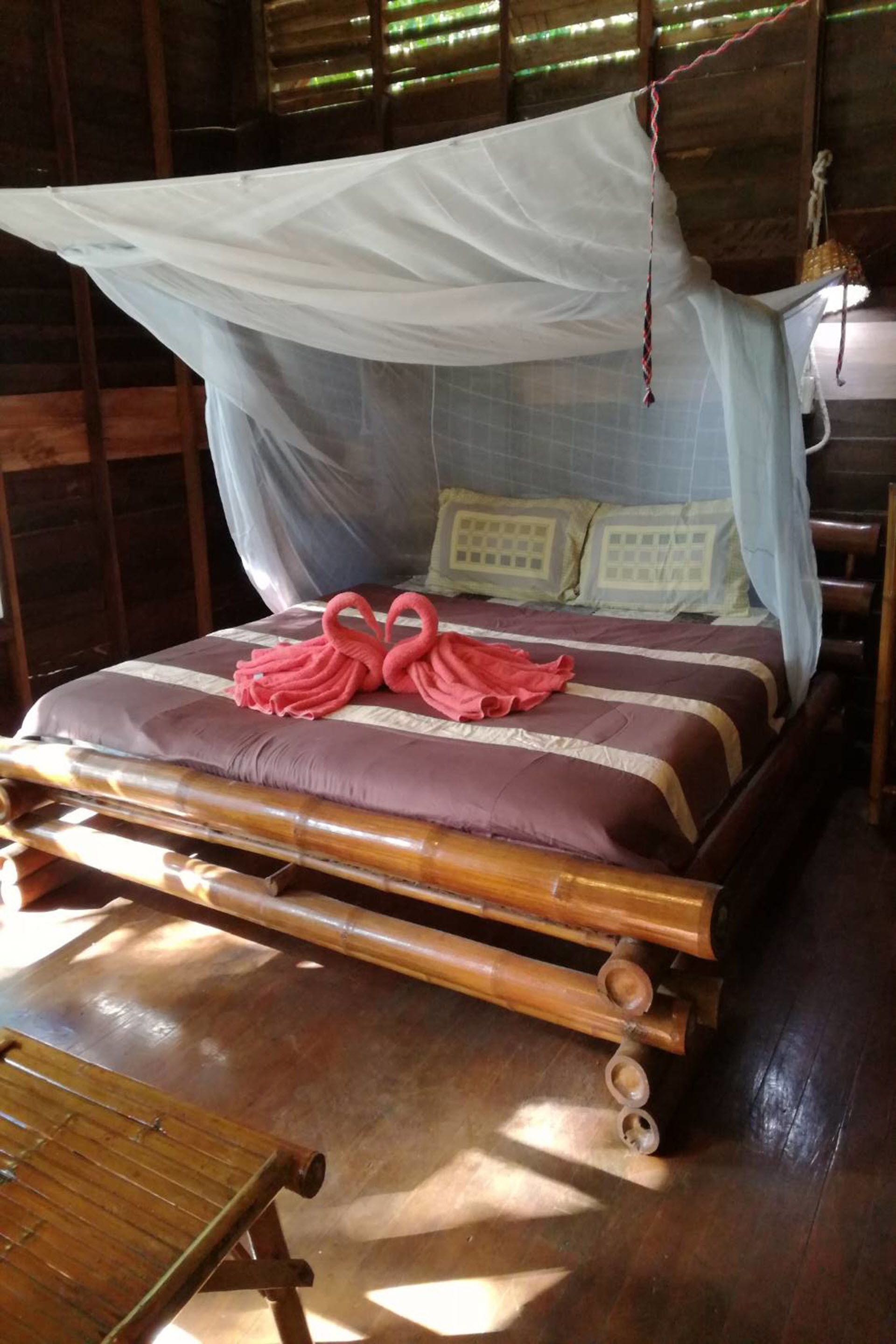 A bed with a mosquito net, two pink towels, and a wooden headboard.