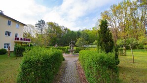 A garden with a stone pathway leading to a central fountain, surrounded by well-maintained hedges and trees. - 207 - Hotel Dunenschloss (Karlshagen)