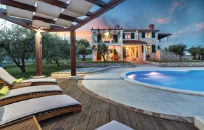 Una casa de dos pisos con piscina, terraza de madera y zona de estar al aire libre.